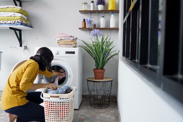 Frau vor der Waschmaschine, die einige Wäsche macht, die Kleidung nach innen lädt