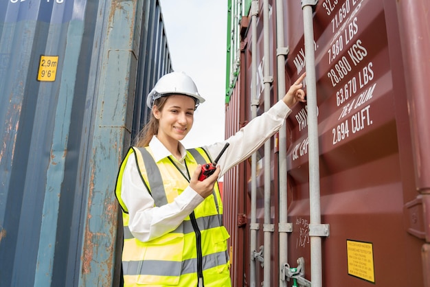 Frau Vorarbeiter lächelt mit Walkie-Talkie vor Frachtgabelstapler im Lager Manager in weißem Helm Sicherheitsbeauftragter im Container Custom Terminal Hafenkonzept Import Export