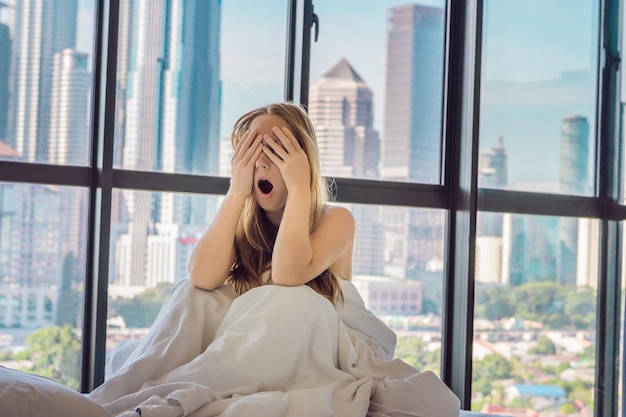 Frau wacht morgens in einer Wohnung in der Innenstadt mit Blick auf die Hochhäuser auf. Leben im Lärm des Großstadtkonzepts. Nicht genug Schlaf