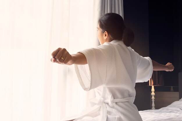 Frau wachte morgens auf und streckte ihre Arme im modernen Bettraum aus.