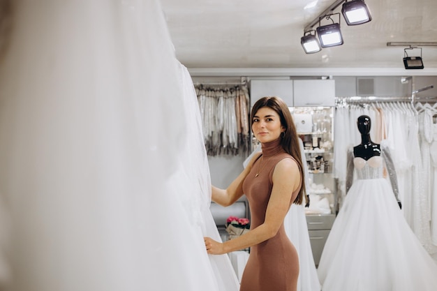 Frau wählt Hochzeitskleid in einem Ausstellungsraum Zukünftige Braut kauft ein Hochzeitskleid in einem Geschäft