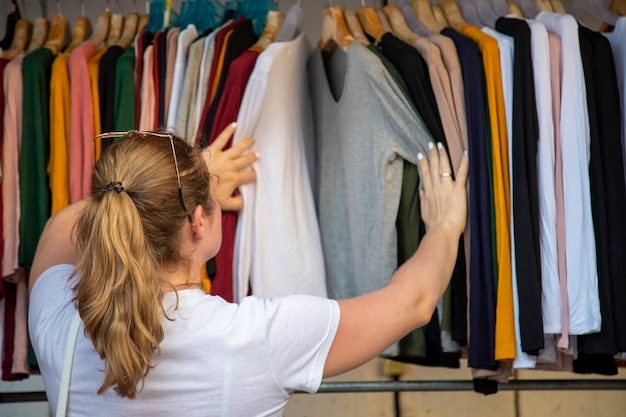 Frau wählt Kleidung durch den Sender im Laden auf dem Markt. Rückansicht