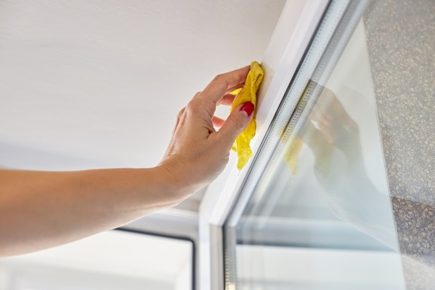 Frau wäscht den Rahmen des offenen Fensters mit gelbem Lappen