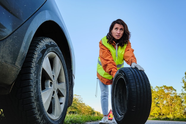 Frau wechselt das beschädigte Rad des Autos