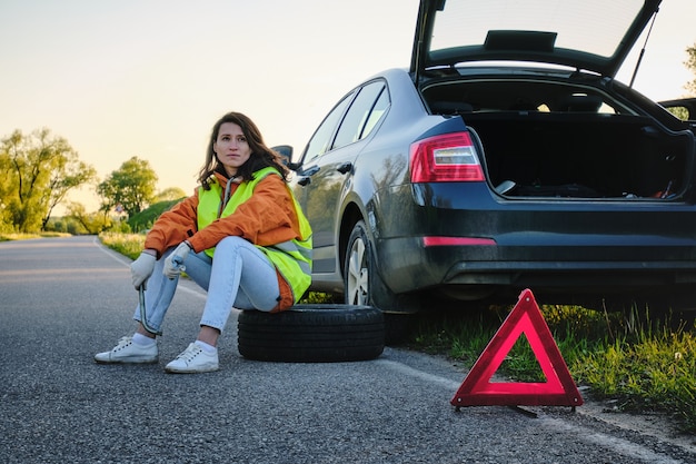 Frau wechselt das beschädigte Rad des Autos