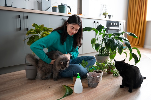 Frau wechselt während der Quarantäne die Töpfe ihrer Pflanzen und streichelt ihre Katzen zu Hause