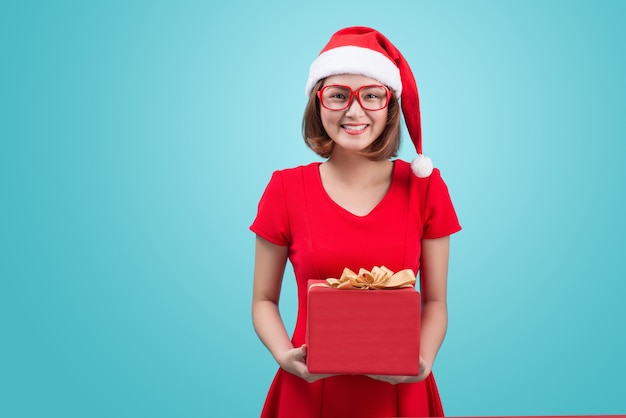 Frau Weihnachtsmann. Schöne junge asiatische Frau in Sankt-Hut, der ein Geschenk lokalisiert auf Blau hält.