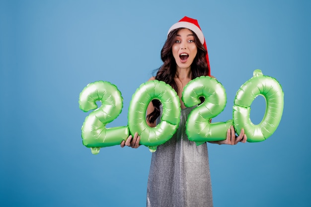Frau, welche die 2020 Ballone des neuen Jahres tragen Weihnachtshut und -kleid hält