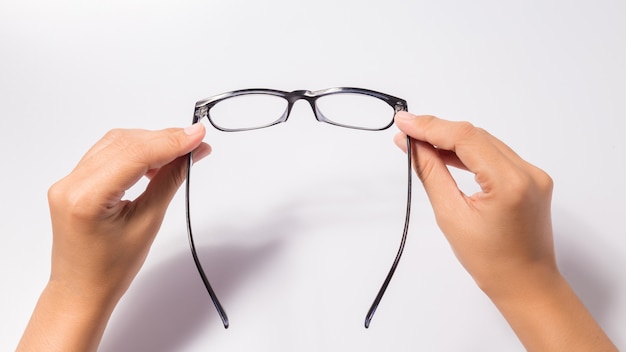 Frau, welche die Brillengläser des schwarzen Auges mit dem glänzenden schwarzen Rahmen lokalisiert auf Weiß hält