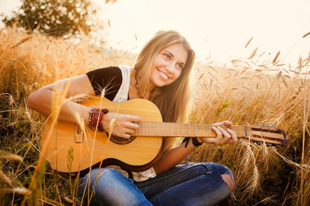 Frau, welche die Gitarre auf einem Weizengebiet spielt