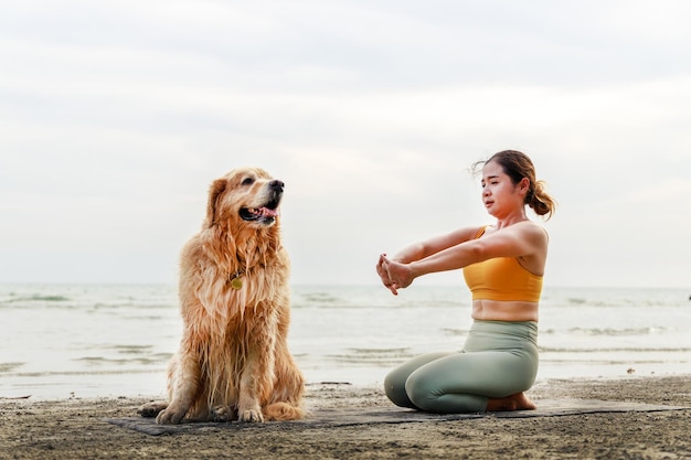 Frau Yoga-Übungen am Strand mit ihrem süßen Hund Gesundes, aktives Lifestyle-Konzept Entspannung mit einem Haustier