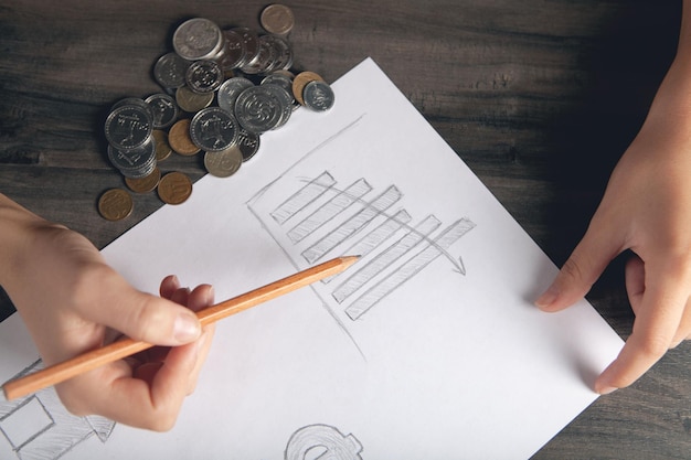 Frau zeichnet ein Diagramm auf Papier und Münzen auf dem Tisch
