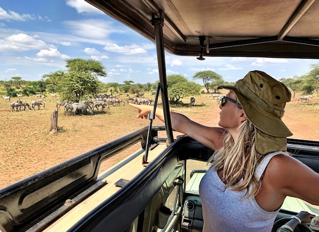 Foto frau zeigt auf zebras auf dem land von einem autodach gegen den himmel