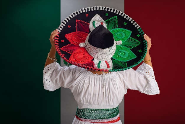 Frau zeigt mexikanischen Hut mit den Farben der mexikanischen Flagge Mexikanische Flagge im Hintergrund