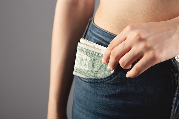 Frau zieht Geld aus der Tasche auf grauem Hintergrund