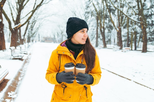 Frau zu Fuß durch verschneiten Stadtpark mit Kaffeetasse. Konzept für kalte Tage aufwärmen