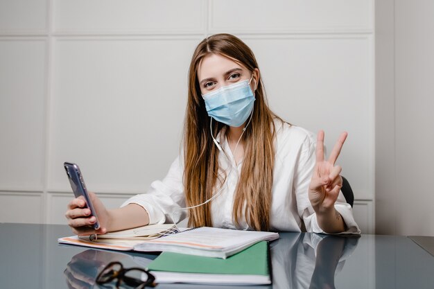 Frau zu Hause Büro mit Laptop tragen Maske und lernen online mit Studienbüchern und Telefon