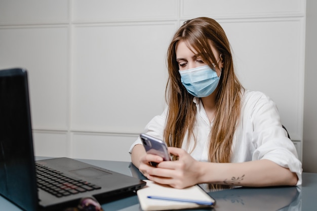 Frau zu Hause Büro mit Laptop tragen Maske und mit Telefon