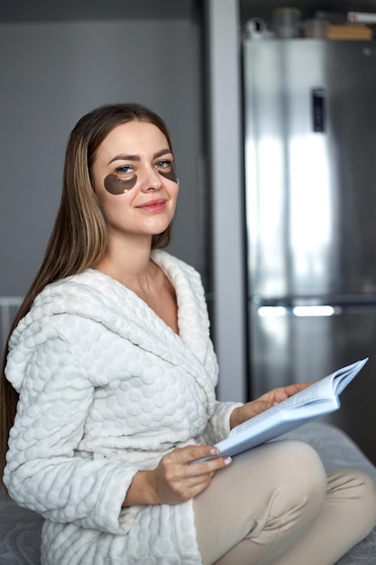 Foto frau zu hause, die ein buch liest und schwarze augenpflaster trägt kosmetologie und hautpflege