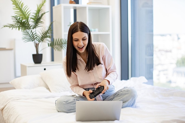 Frau zu Hause im Bett und benutzt einen modernen drahtlosen Joystick, um Spiele zu spielen