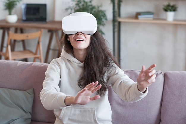 Frau zu Hause mit Virtual-Reality-Headset, das Spiel auf dem Sofa spielt