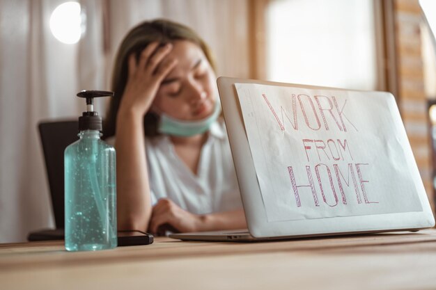 Frauen arbeiten von zu Hause aus mit Maskenschutz und warten darauf, dass sich die epidemische Situation zu Hause bald verbessert. Coronavirus, Covid-19, Arbeit von zu Hause aus (WFH), soziale Distanzierung, Quarantäne, Konzept zur Infektionsprävention.