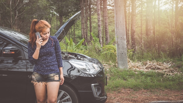 Frauen benutzen das Telefon, um kaputtes Auto zu kontaktieren.