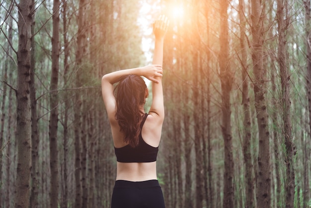 Frauen, die Arme ausdehnen und frische Luft im Kiefernwald beim Trainieren atmen