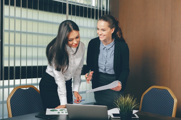 Frauen, die bei Tisch Finanzdokumente im Laptop schauen