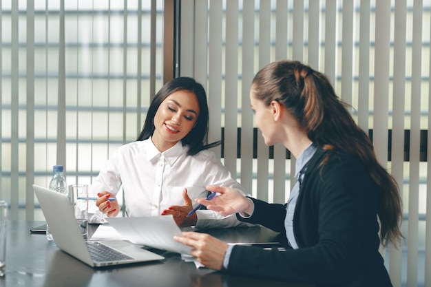 Frauen, die bei Tisch Finanzdokumente im Laptop schauen