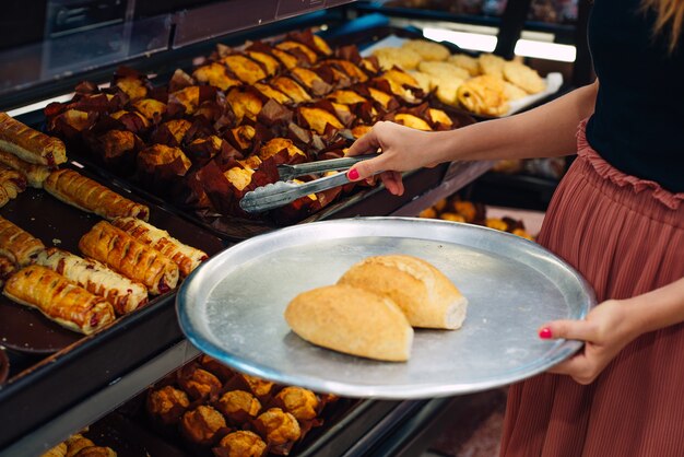 Frauen, die Brot im Supermarkt wählen Brötchenzange und Tablett.