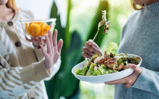 Frauen, die sich dafür entscheiden, Kartoffelchips zu essen, und mit den Händen zeigen, dass sie eine Person mit Gemüsesalat ablehnen