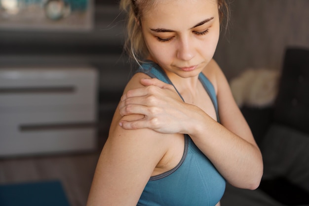 Foto frauen, die sportanzüge tragen, fühlen schulterschmerzen nach dem training zu hause