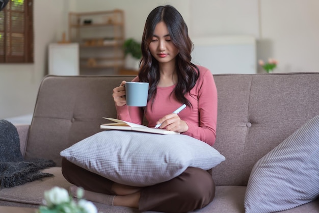 Frauen entspannen sich auf dem Sofa, trinken Kaffee und schreiben Notizen auf dem Tagebuch im Lebensstil zu Hause