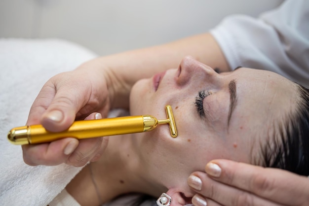 Frauen erhalten im Spa eine Pulsmassage mit goldenem Gesichtsmassagegerät auf dem weiblichen Gesicht