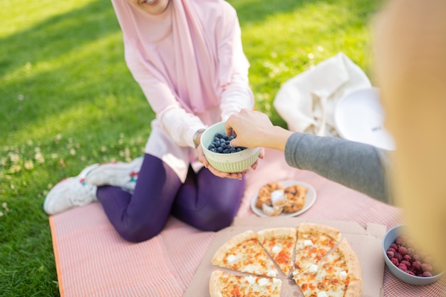 Frauen essen Blaubeeren. Draufsicht auf Frauen, die im Sommer Blaubeeren essen, während sie auf Gras sitzen?