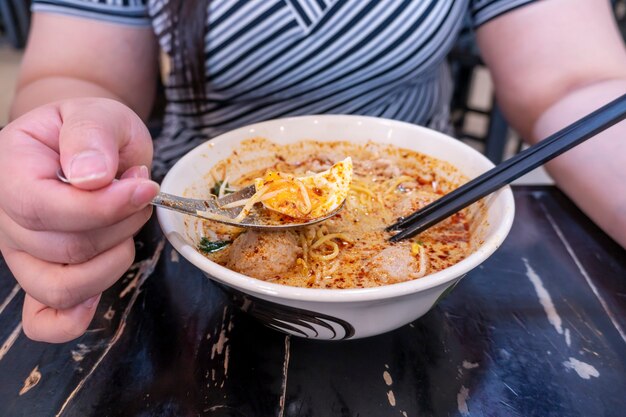 Frauen essen Schweinefleischnudeln Tom Yum mit Ei auf verschwommenem Holztisch