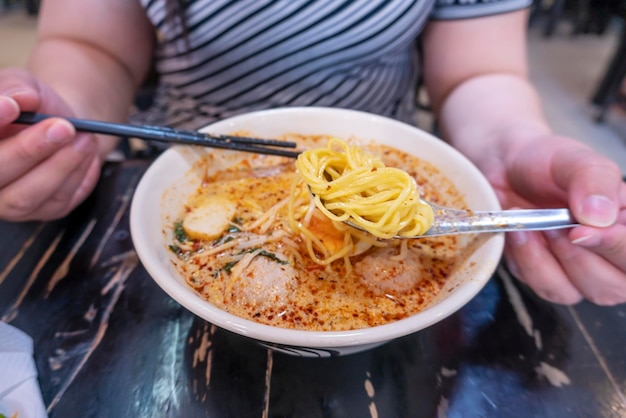 Frauen essen Schweinefleischnudeln Tom Yum mit Ei auf verschwommenem Holztisch