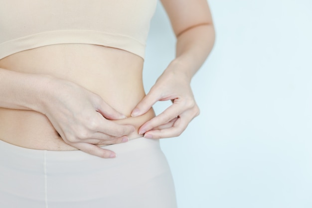 Frauen fangen Fett am Bauch, um zu sehen, wie sie den Bauch reduziert. Mädchen, das fette Schicht auf Taille prüft