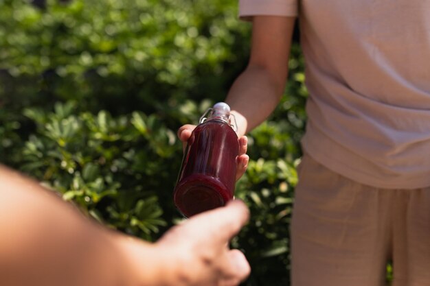 Frauen geben eine Glasflasche mit nahrhaftem Saftgetränk mit Pflanzenblatthintergrund