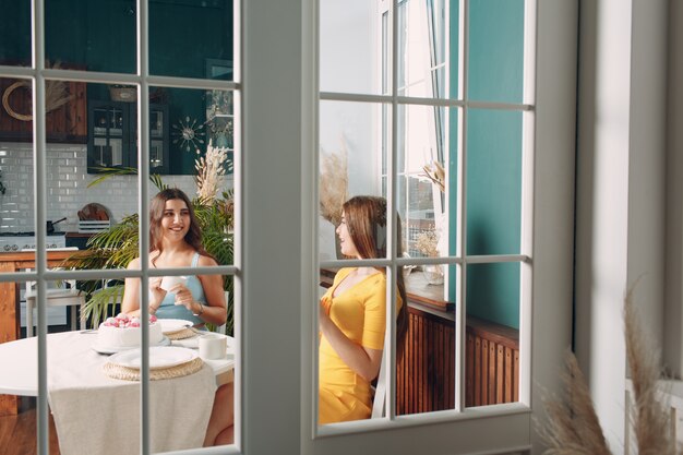 Frauen glückliche Freunde zu Hause sitzen und lächeln mit weißem Geburtstagskuchen hinter Glastür.