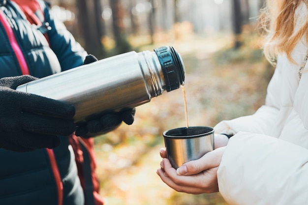 Foto frauen haben eine pause während einer herbstreise und gießen an einem kalten herbsttag ein heißes getränk aus einer thermosflasche.