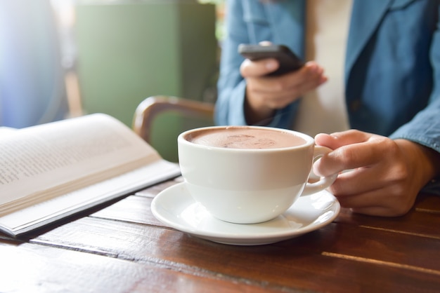 Frauen-Hände, die Tasse Kaffee halten und intelligentes Telefon verwenden.