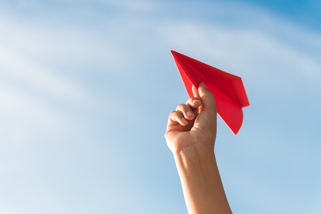 Frauen-Hand, die rote Papierrakete mit Hintergrund des blauen Himmels hält.