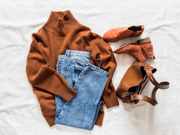 Frauen Herbst Frühlingszeit Kleidung Kaschmir brauner Pullover Suede Chelsea blaue Mom Jeans und eine Leder Tasche auf einer leichten Oberfläche