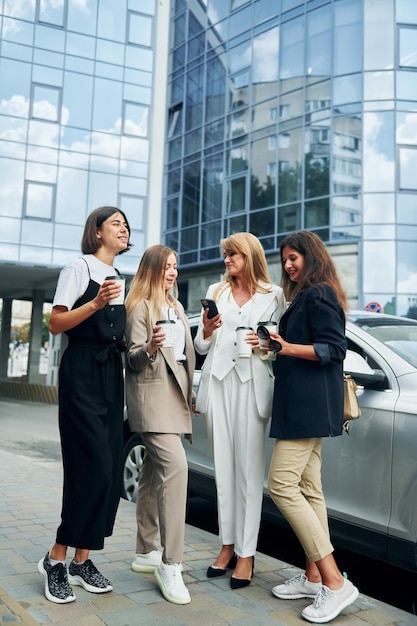 Frauen in formeller Kleidung stehen draußen in der Stadt zusammen in der Nähe eines silberfarbenen Autos