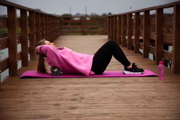 Foto frauen in rosafarbenem hoodie, die im herbst übungen im freien am pier machen