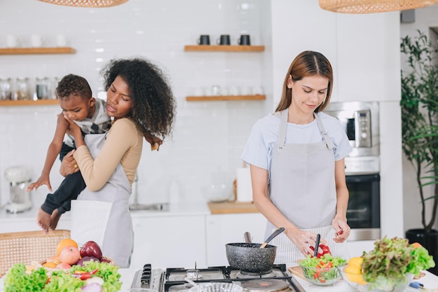 Frauen kochen auf einer Party das Essen bei einem Freund zu Hause, Küchenurlaub mit verspielter Kinderbetreuung für ihren Sohn