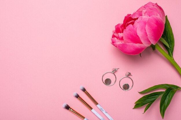 Frauen Make-up Pinsel und Ohrringe mit einer schönen Blumenpfingstrose mit Kopierraum für Ihren Text