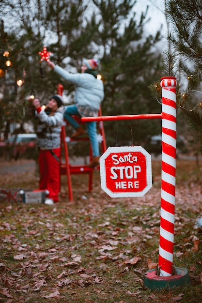 Foto frauen schmücken einen weihnachtsbaum im freien wunderkerze leuchtet ein stoppschild mit dem text santa stop hier